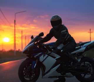 Pessoa a andar de mota com o pôr do sol atrás