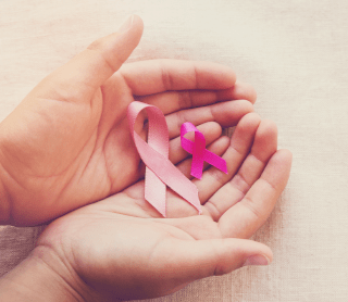 Duas mãos em forma de concha a segurar dois laços cor-de-rosa