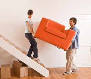 Casal a carregar um sofá enquanto descem as escadas de casa 