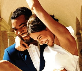 Um casal de recém-casados sorridentes festeja num corredor de pedra.