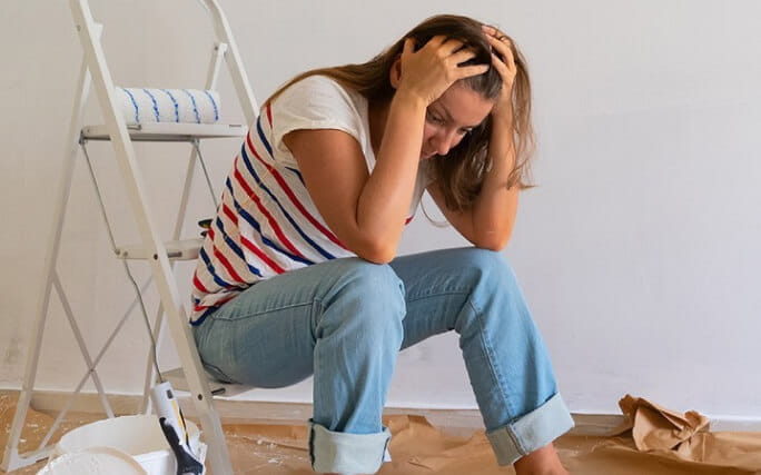 Mulher sentada num escadote de degraus desesperada com os atrasos de obras em casa. 