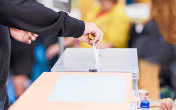 Pessoa não identificada coloca o seu voto dentro de uma urna de voto.