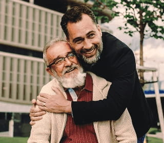 Homem a abraçar carinhosamente um homem mais velho que está sentado num banco de jardim.