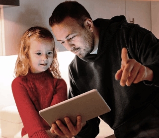 Pai e filha a observar conteúdo num tablet numa cozinha iluminada.