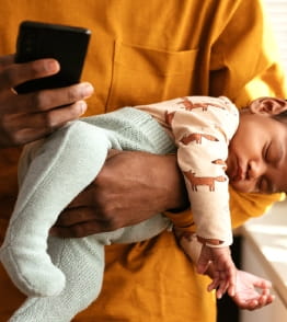 Pai a segurar um bebé adormecido enquanto utiliza o telemóvel.
