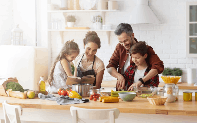 Pai, mãe e dois filhos pequenos preparam uma refeição em família numa ambiente feliz e descontraído.
