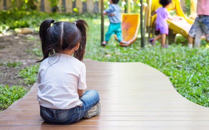Uma menina com ansiedade infantil sentada sozinha no recreio da escola.