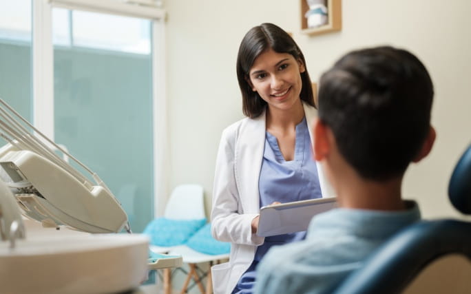 Menino sentado numa cadeira de dentista, enquanto a médica dentista faz um check-up dentário.