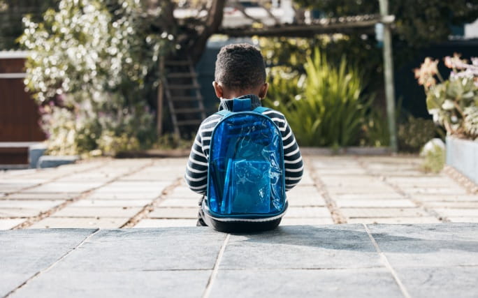 Criança autista, sentada num jardim, sozinha e isolada.