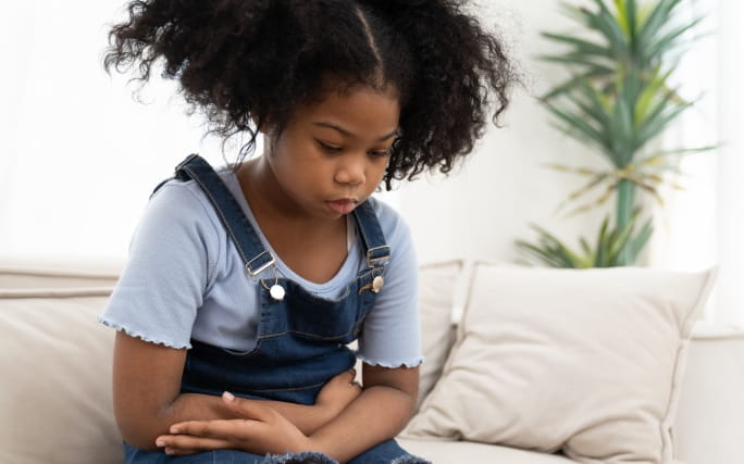 Menina sentada num sofá agarrada à barriga com sintomas gastroenterite infantil.