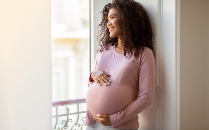 Mulher jovem grávida e feliz ampara a barriga com as mãos.