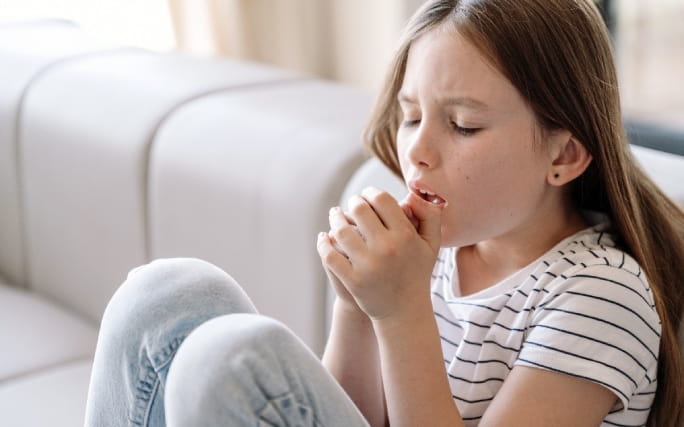 Menina sentada num sofá com um ataque de tosse.