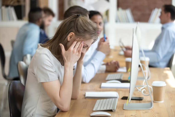 Mulher sentada na secretária, à frente do computador, no escritório.