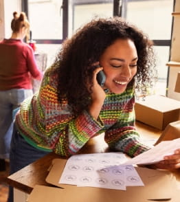 Mulher empreendedora a falar ao telefone enquanto verifica encomendas numa loja de roupa.